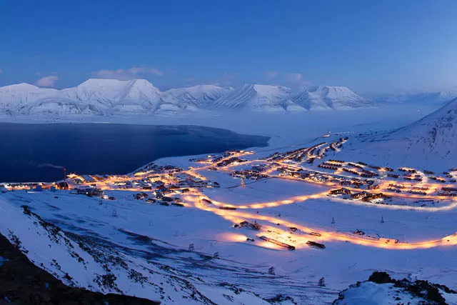 lights lit up in residential area between snow covered hill at dusk in svalbard, norway