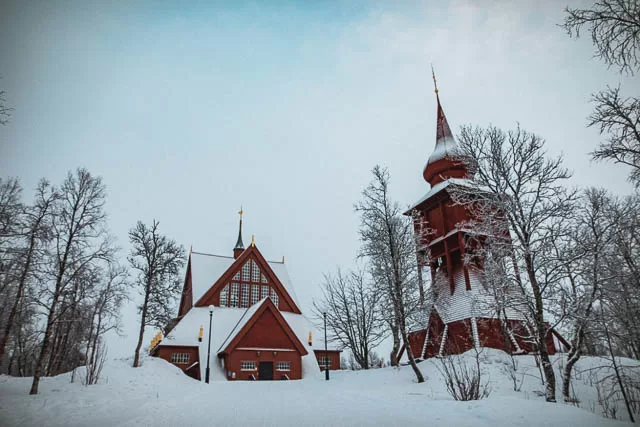 dry trees in front of snow covered jukkasjärvi church, sweden